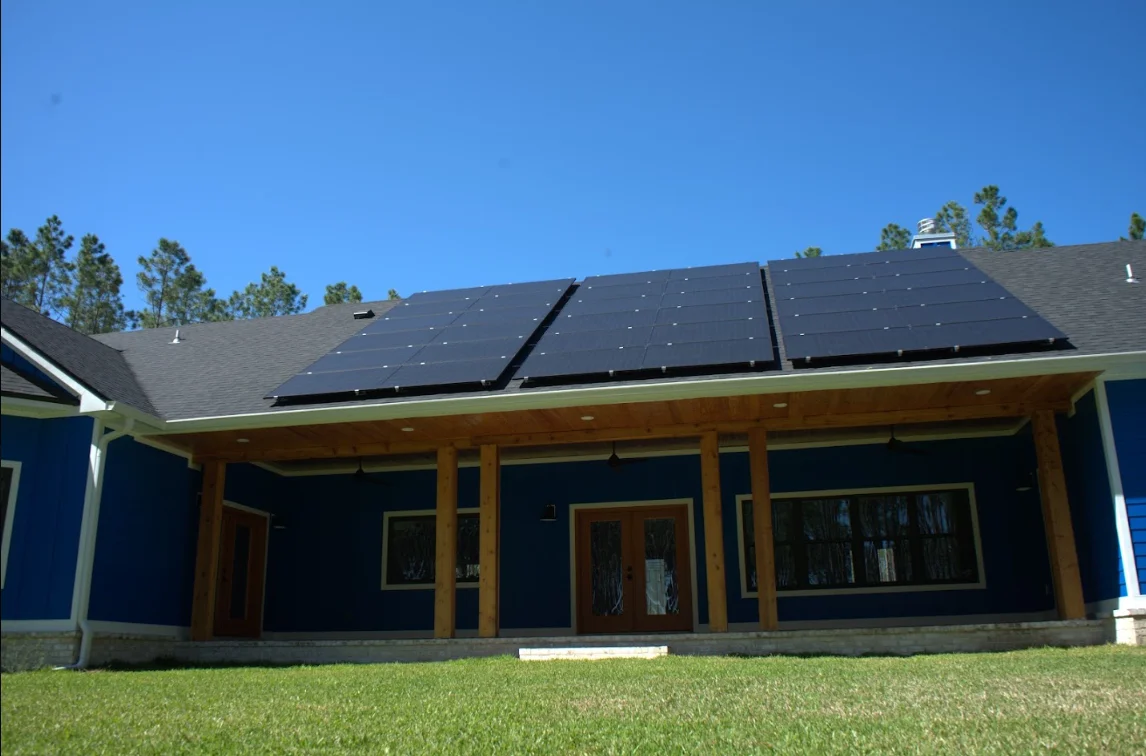 Solar panels installed on residential roof with wooden patio structure and blue siding
