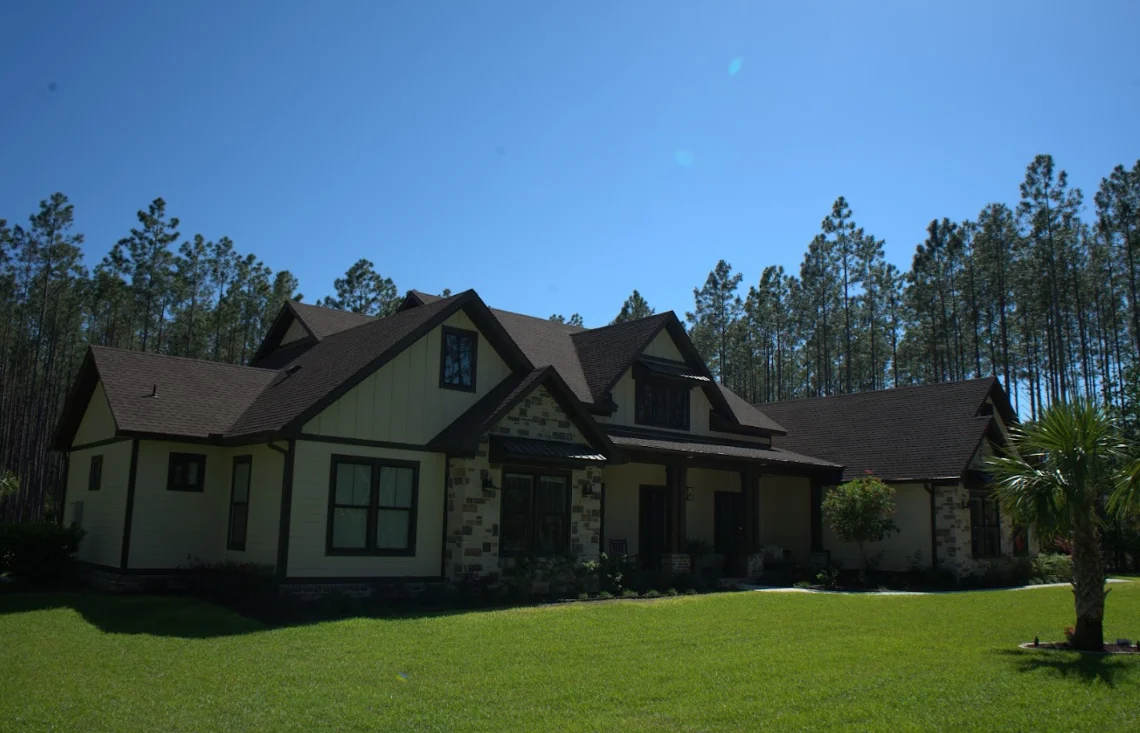 Dark gray architectural shingle roof on two-story home with stone accents and pine trees