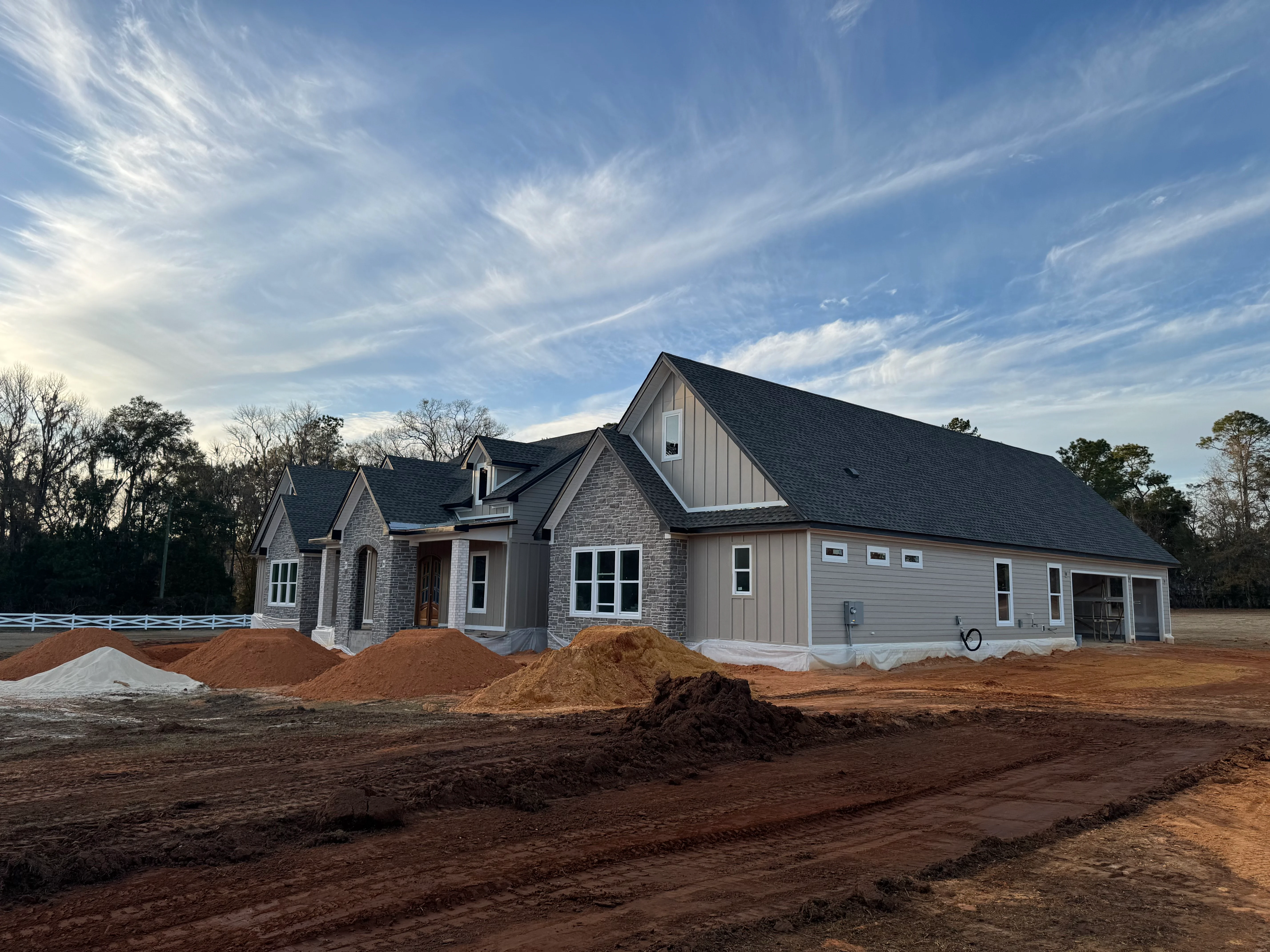 New home with dark asphalt shingle roof installation, multiple gables, and construction site with material piles