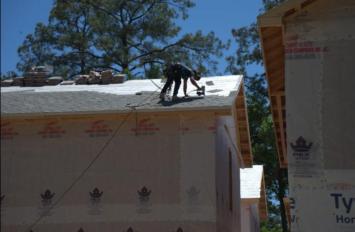 Roofer installing architectural shingles on residential roof with house wrap underlayment