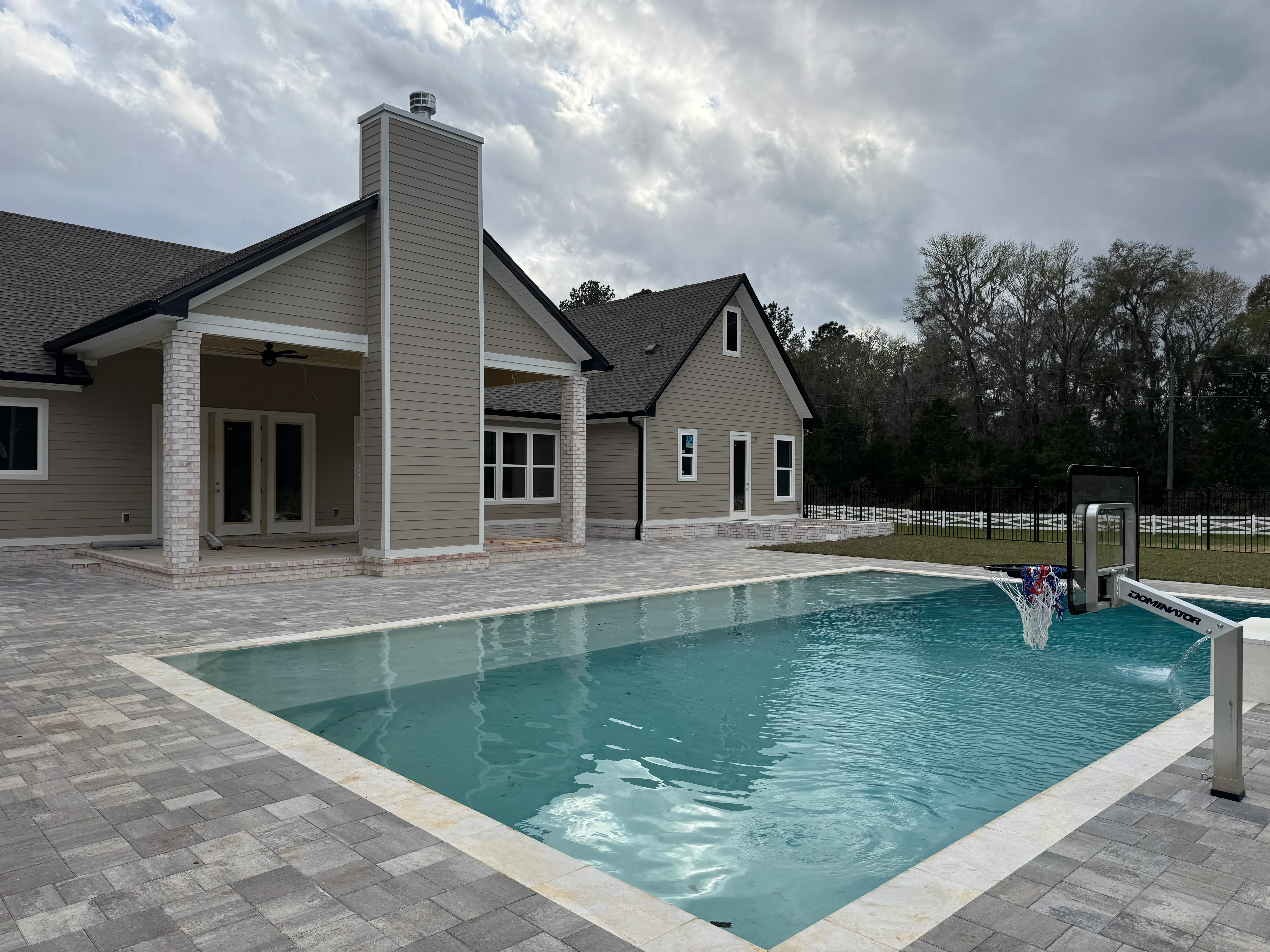 Modern home with multi-pitched gray asphalt shingle roof and brick chimney overlooking pool