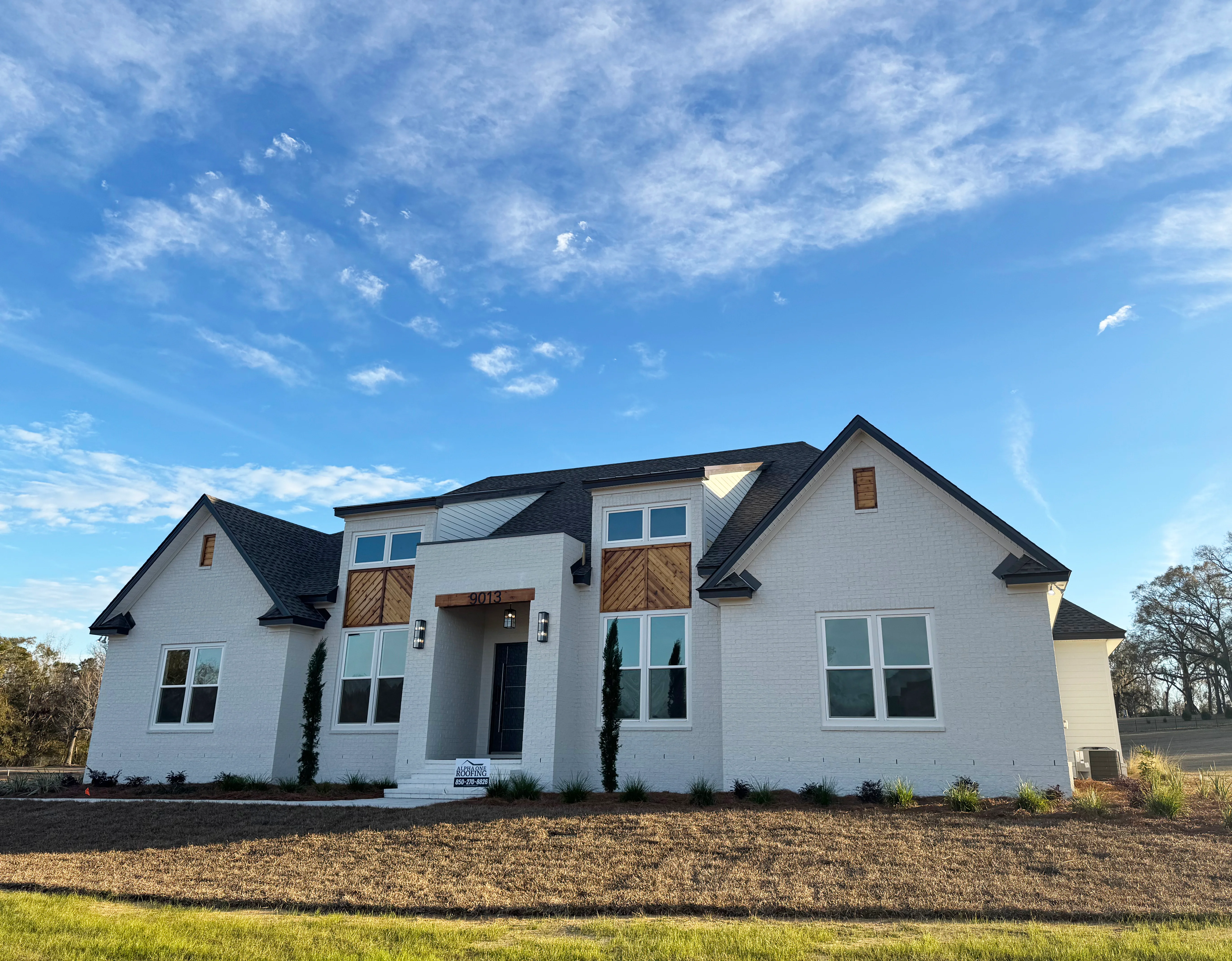White brick home with dark shingle roof installation and metal roof accents in Tallahassee