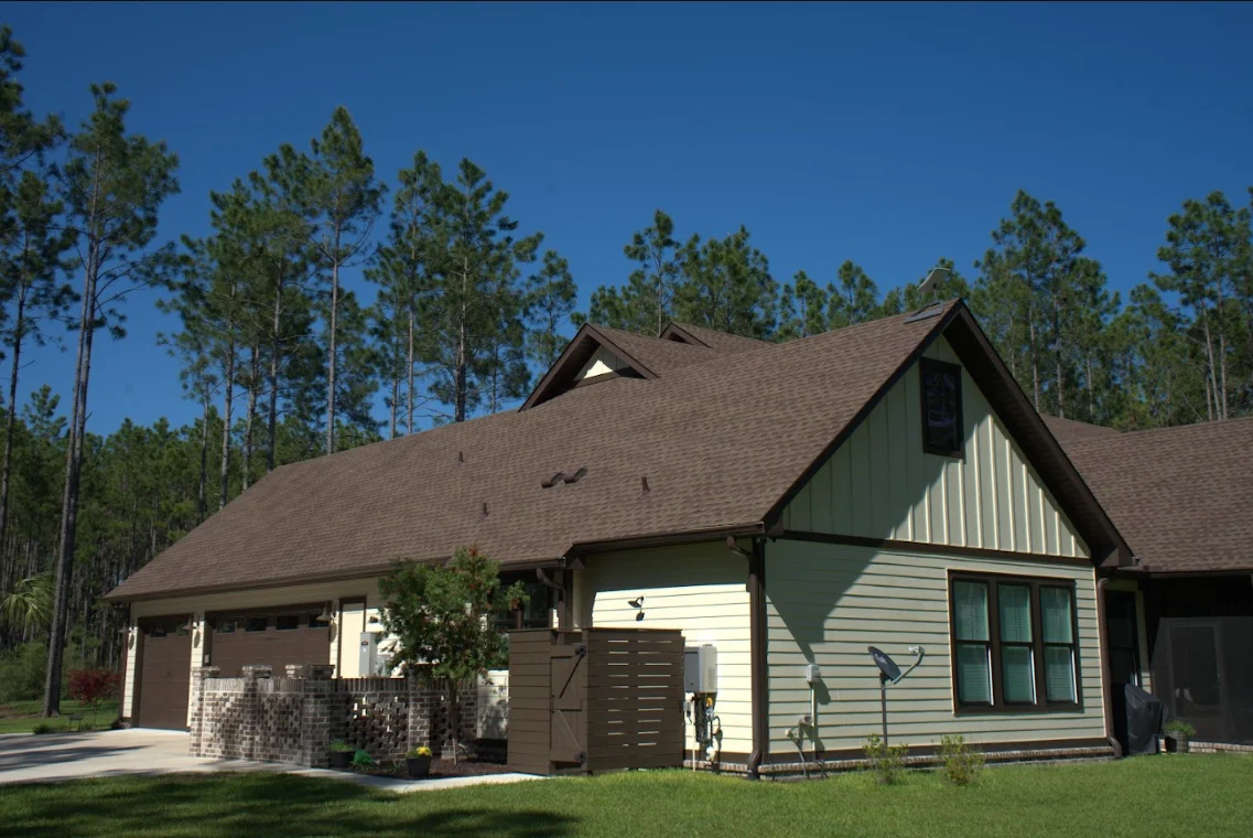 Brown asphalt shingle roof on residential home with gable design and pine trees