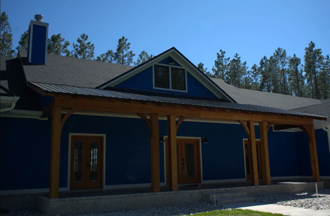 Modern home with gray shingle roof, metal gable accent, and timber-framed porch