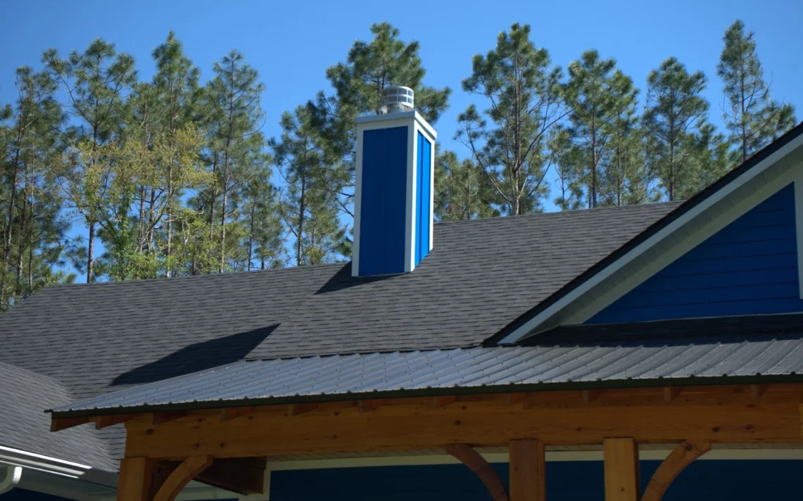Modern home with gray asphalt shingle roof and blue metal chimney against pine trees