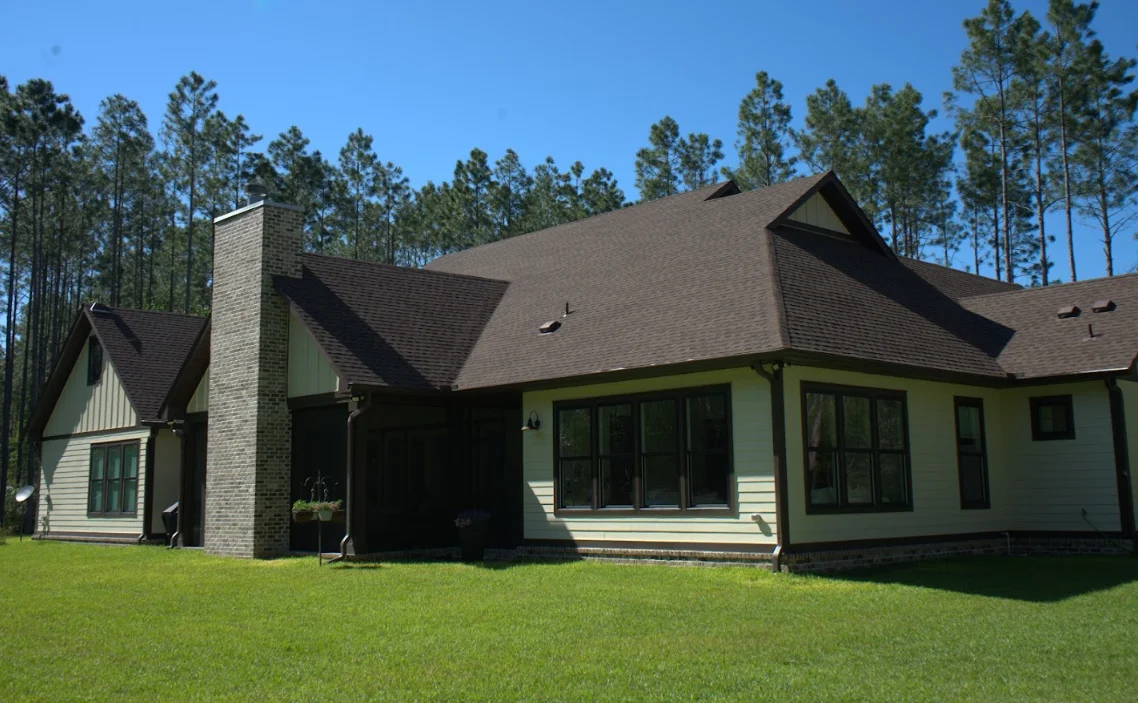 Modern home with new charcoal architectural shingle roof and brick chimney against pine forest backdrop