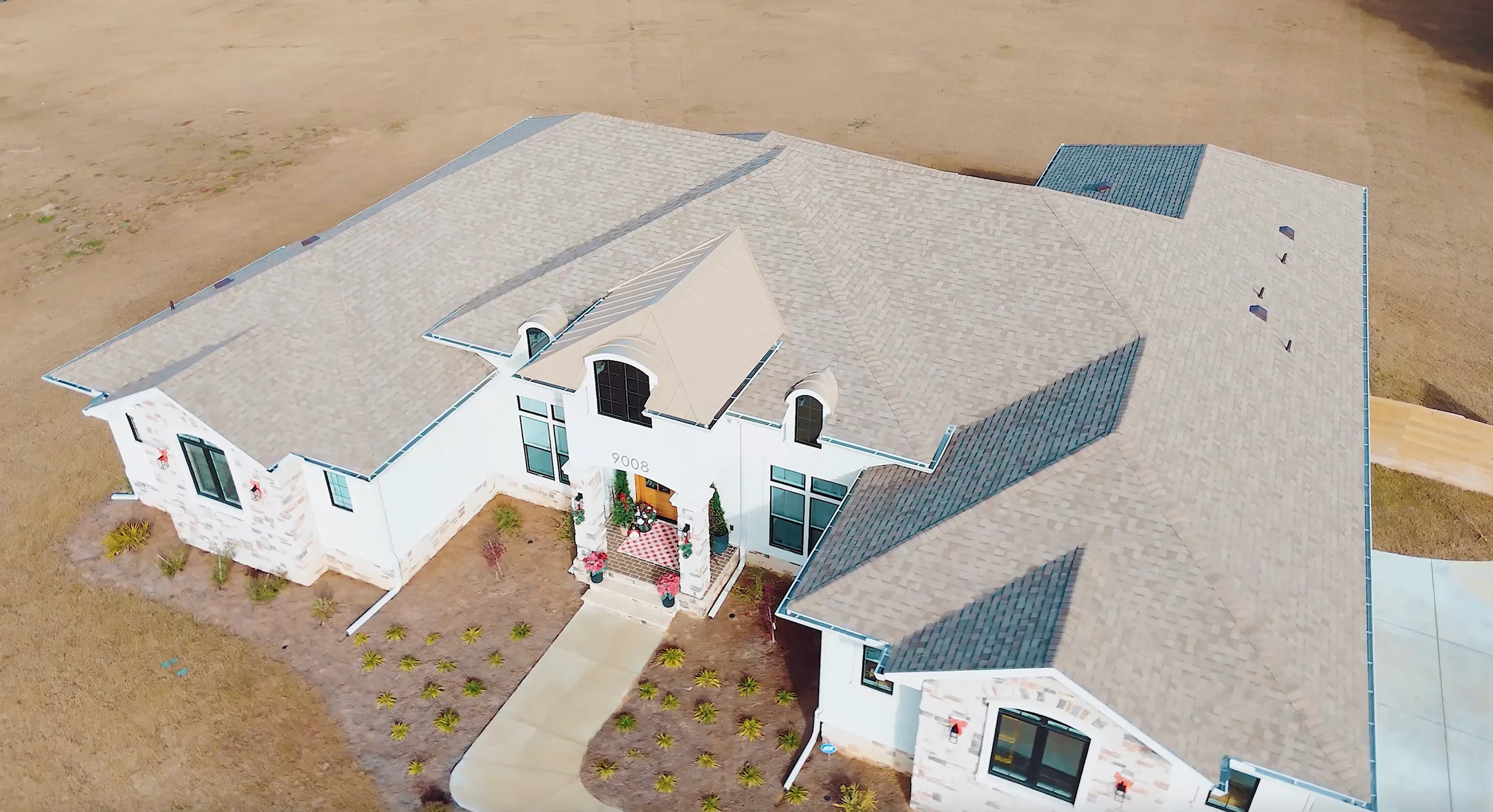 Aerial view of new gray and blue architectural shingle roof installation on white residential home