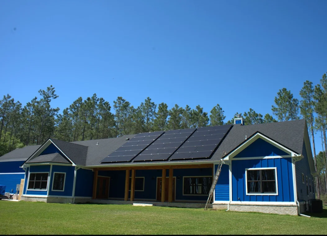 Blue residential home with dark asphalt shingles and solar panels installed on roof